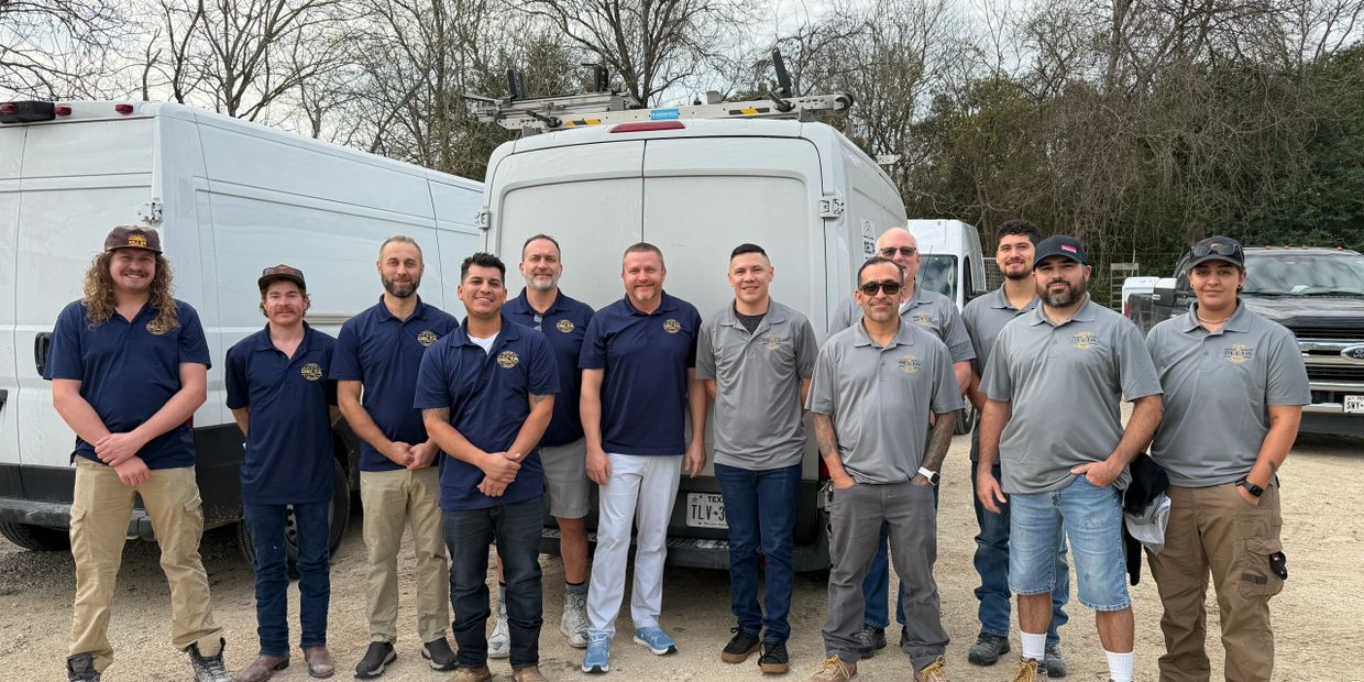 A group of workers in matching shirts posing outdoors in front of vans.
