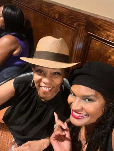 Two women smiling, one wearing a hat and the other a black beret.