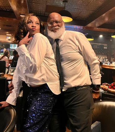 A stylish couple poses playfully in a cozy bar setting.