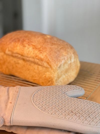 Loaf of sourdough sandwich bread on a cooling rack next to an oven mitt.
