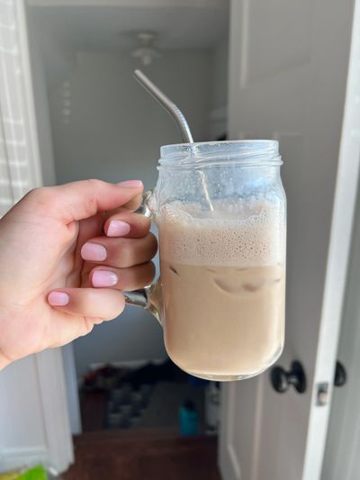 Homemade cookie butter latte in a glass with a being held by a woman's hand with pink nail polish.