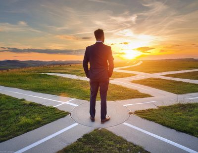 Man in suit standing at crossroads, looking at sunset.