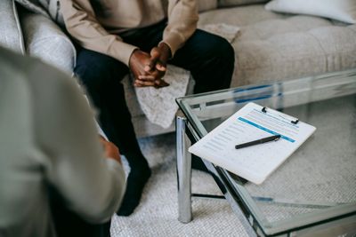 Two people sitting on a couch, looking at a clipboard with pen on a glass coffee table.