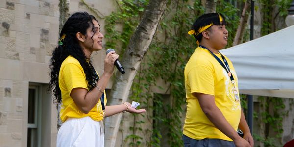 Two people wearing yellow shirts speak outdoors.