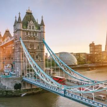 London Bridge spans the River Thames with city buildings in the background on a cloudy day.
