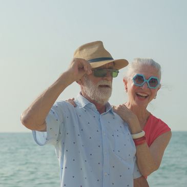 An older couple strolls hand in hand along a sandy beach. 
