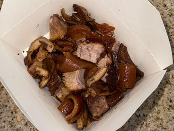 Cooked pork pieces with mushrooms in a takeout container.