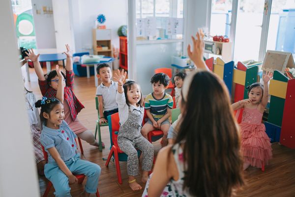 Asian Montessori preschool student raised hands in the class answering questionhand