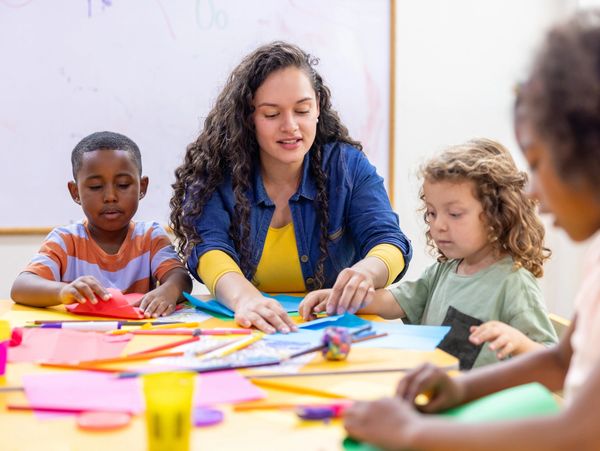Happy preschool teacher helping children while doing crafts in class