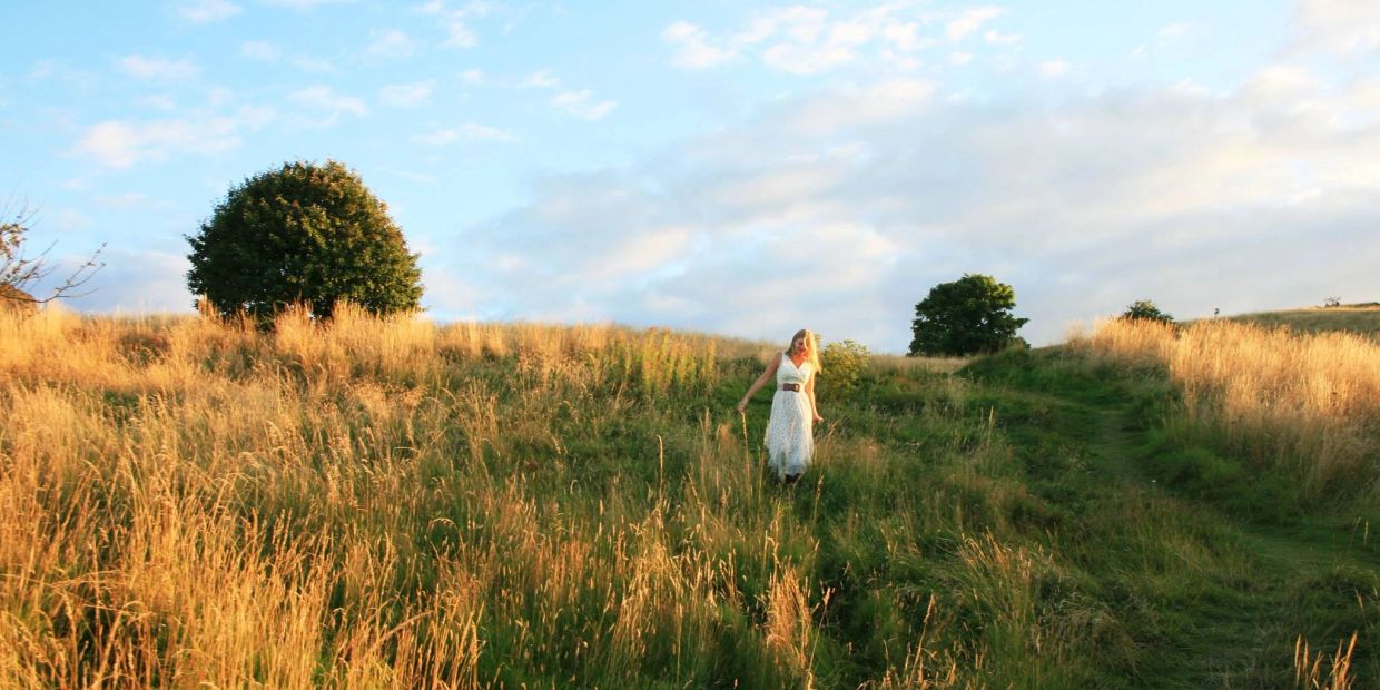 Woman in white dress walking through a grassy field at sunset.