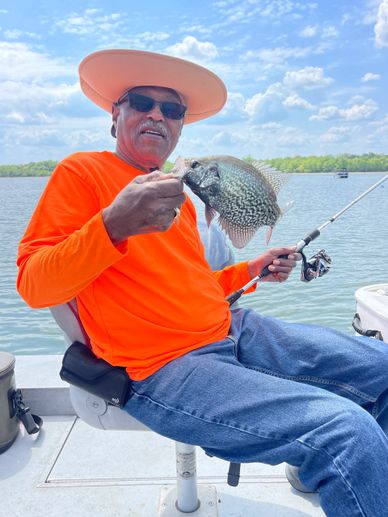 Man in orange shirt holding a fish on a boat under a blue sky.