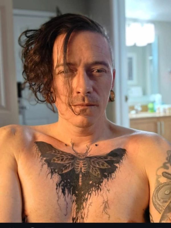 Man with a large butterfly tattoo on chest and curly hair.