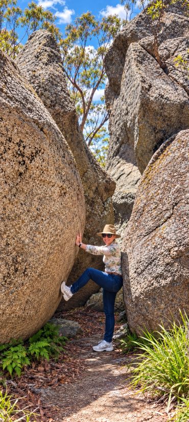 Person posing between large granite boulders on a sunny day.
