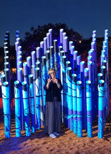 Person standing among blue illuminated tubes at night.