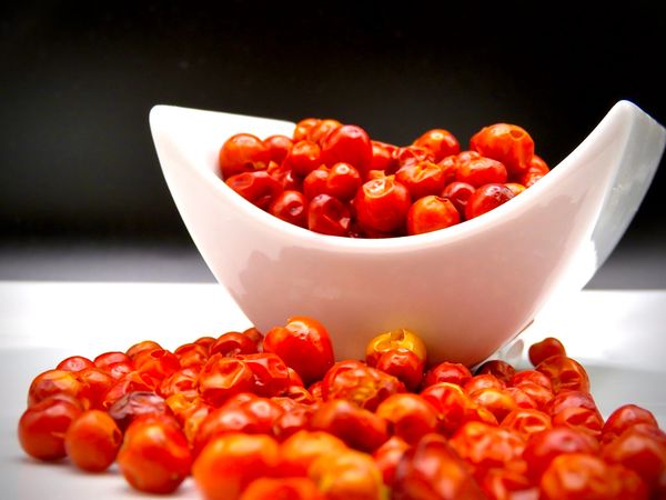 Bright red dried berries in a white bowl with more scattered around it.
