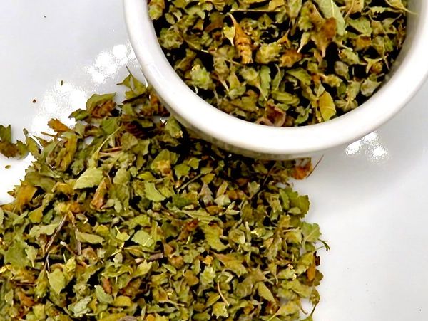 Dried green herbs in a small white bowl on a white plate.
