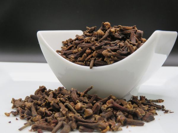 Dried cloves in a white bowl with some spilled on the surface.