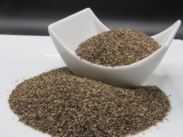 Ground black pepper in a white bowl and spilled on a plate.