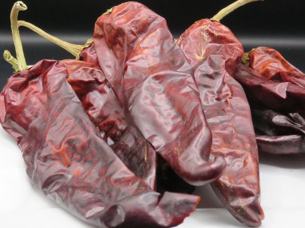 Dried red chili peppers on a white plate with a black background.