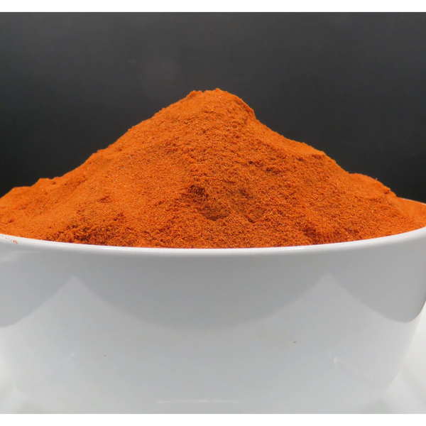 A bowl filled with vibrant red-orange powdered spice against a dark background.
