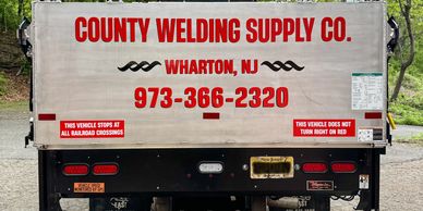 Back of a County Welding Supply Co. truck with contact information and safety notices.