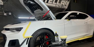 White sports car with open hood in auto care shop, surrounded by detailing tools.
