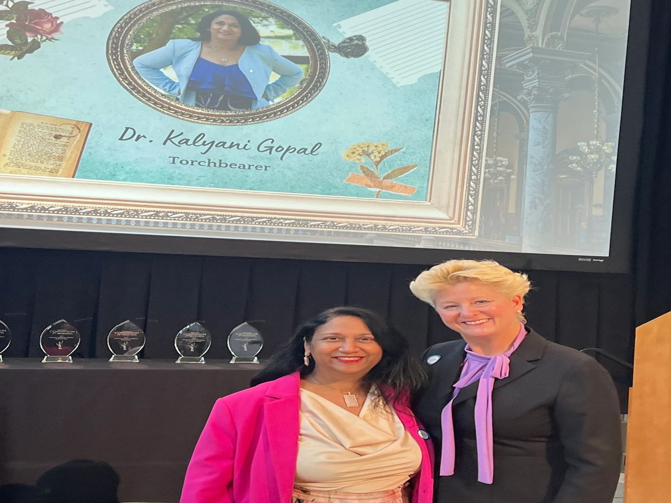 Dr. Kalyani Gopal honored as Torchbearer with a smiling companion at an award event.