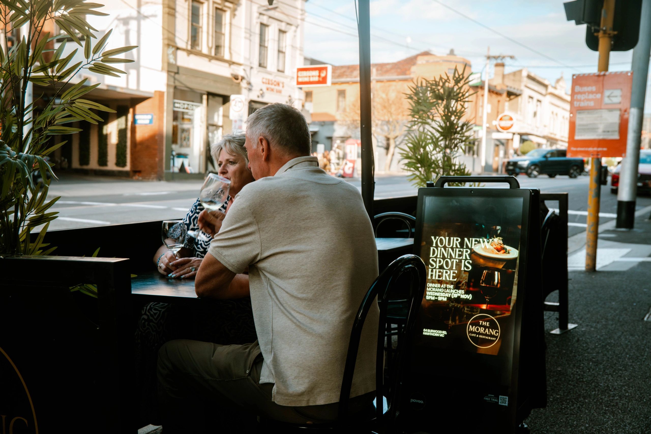 Couple enjoying drinks at an outdoor cafe with a dinner spot advertisement.