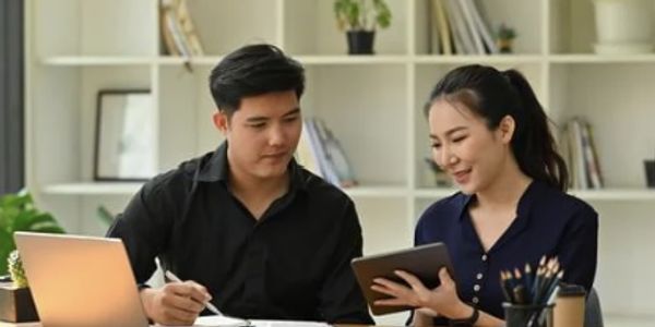 Two colleagues discussing work with a laptop and tablet in an office.