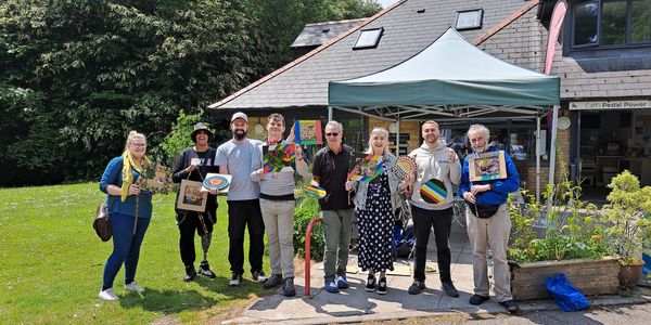 Group of eight people holding colorful artwork outdoors in front of a building.