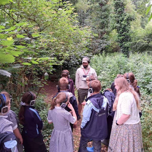 Children wearing headphones listen to a guide in a lush forest.