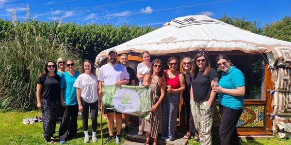 A group of people posing outside a traditional yurt on a sunny day.