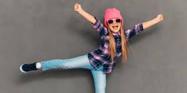 Joyful girl in pink hat and sunglasses posing energetically against a gray background.