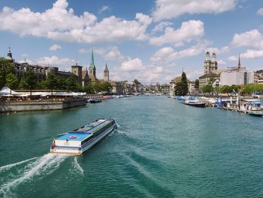 A boat cruising on a river through a historic city under a blue sky.