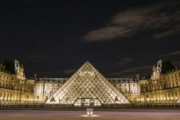 The illuminated Louvre Pyramid shines under a starry night sky in Paris.