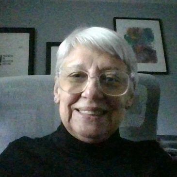 Smiling elderly person with glasses and white hair indoors.