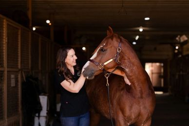 Woman affectionately holding a horse's face in a stable.
