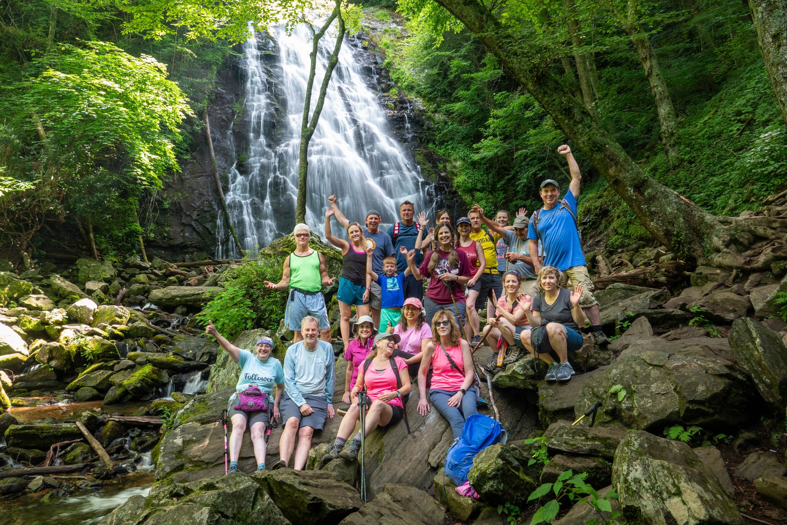 Group of hikers posing joyfully in front of a waterfall in a lush forest.