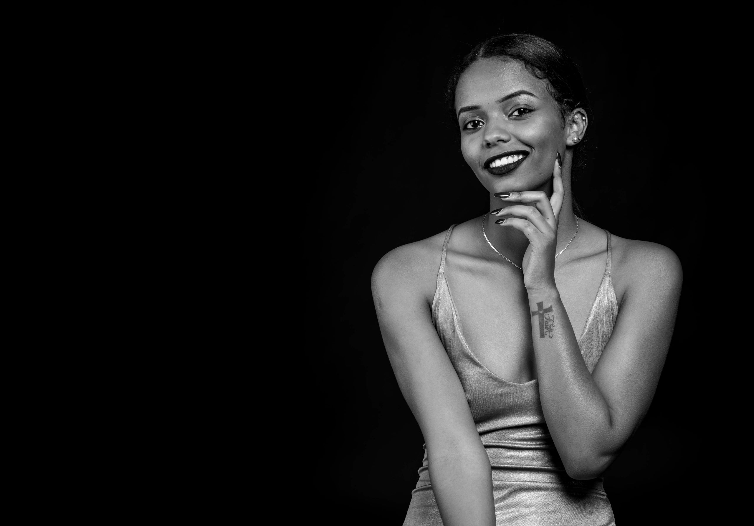 Elegant woman in a satin dress posing against a black background with a confident smile.