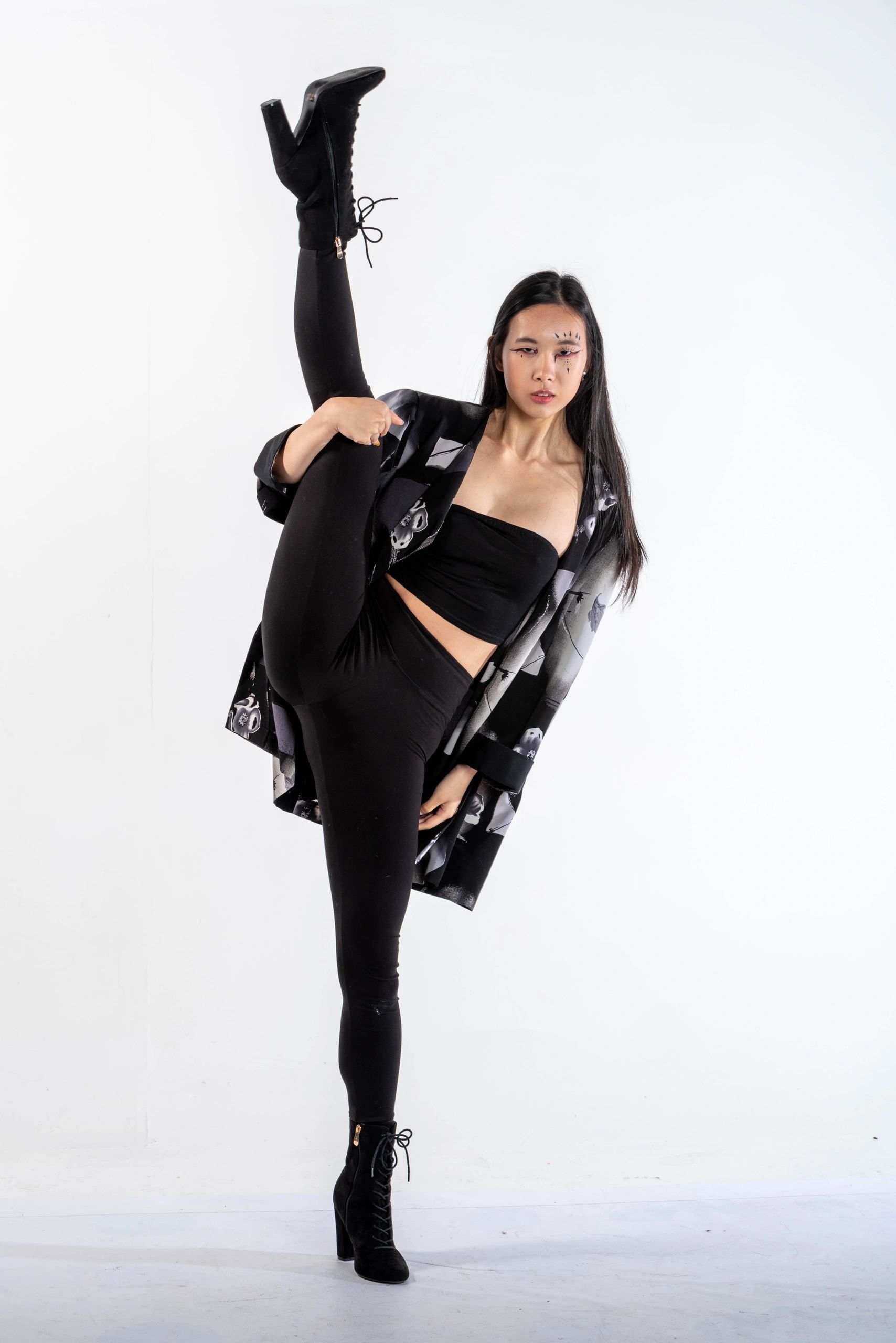 Woman in black outfit performing a high leg stretch against a white background.