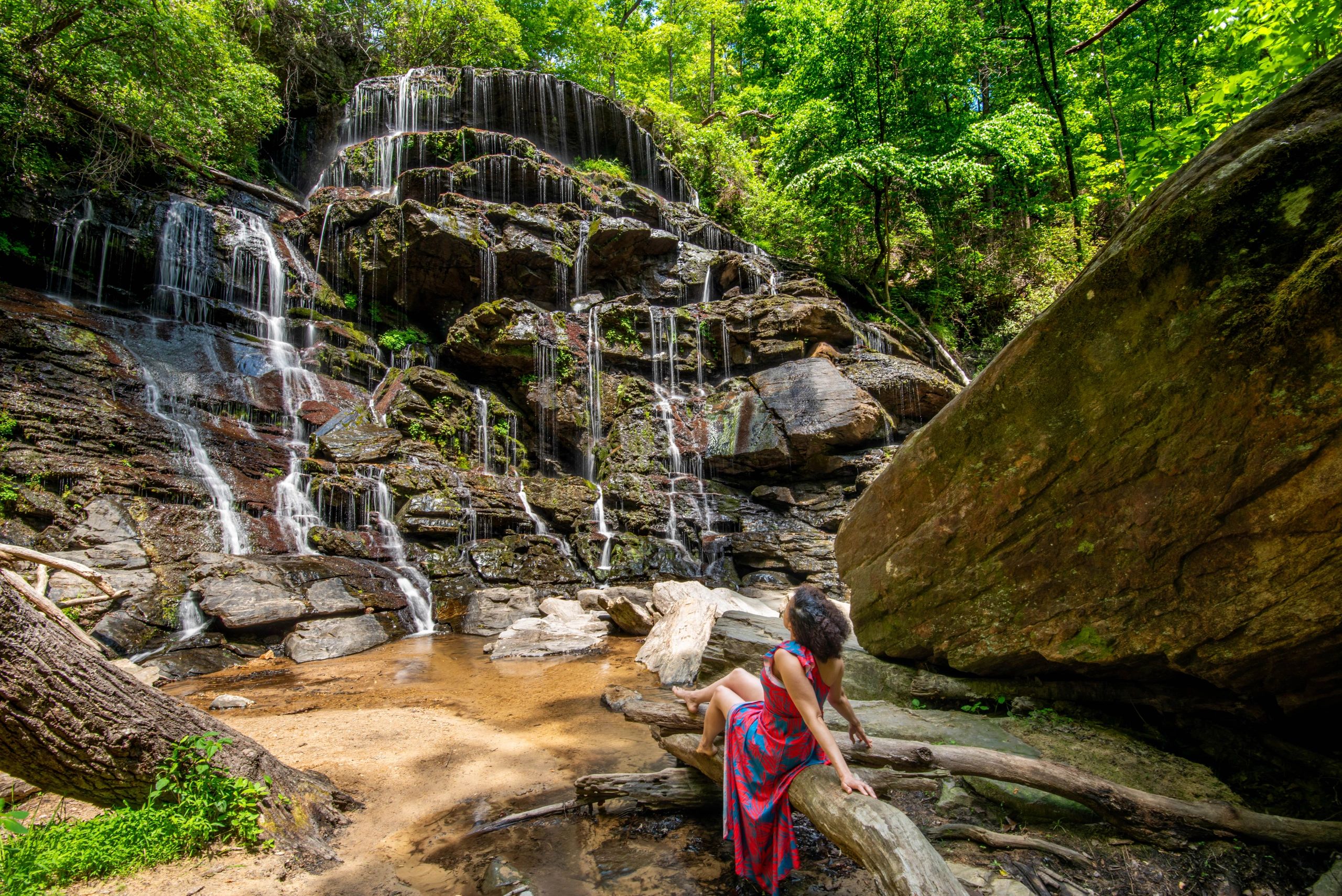 A person in a colorful dress enjoys a peaceful waterfall in a lush forest.