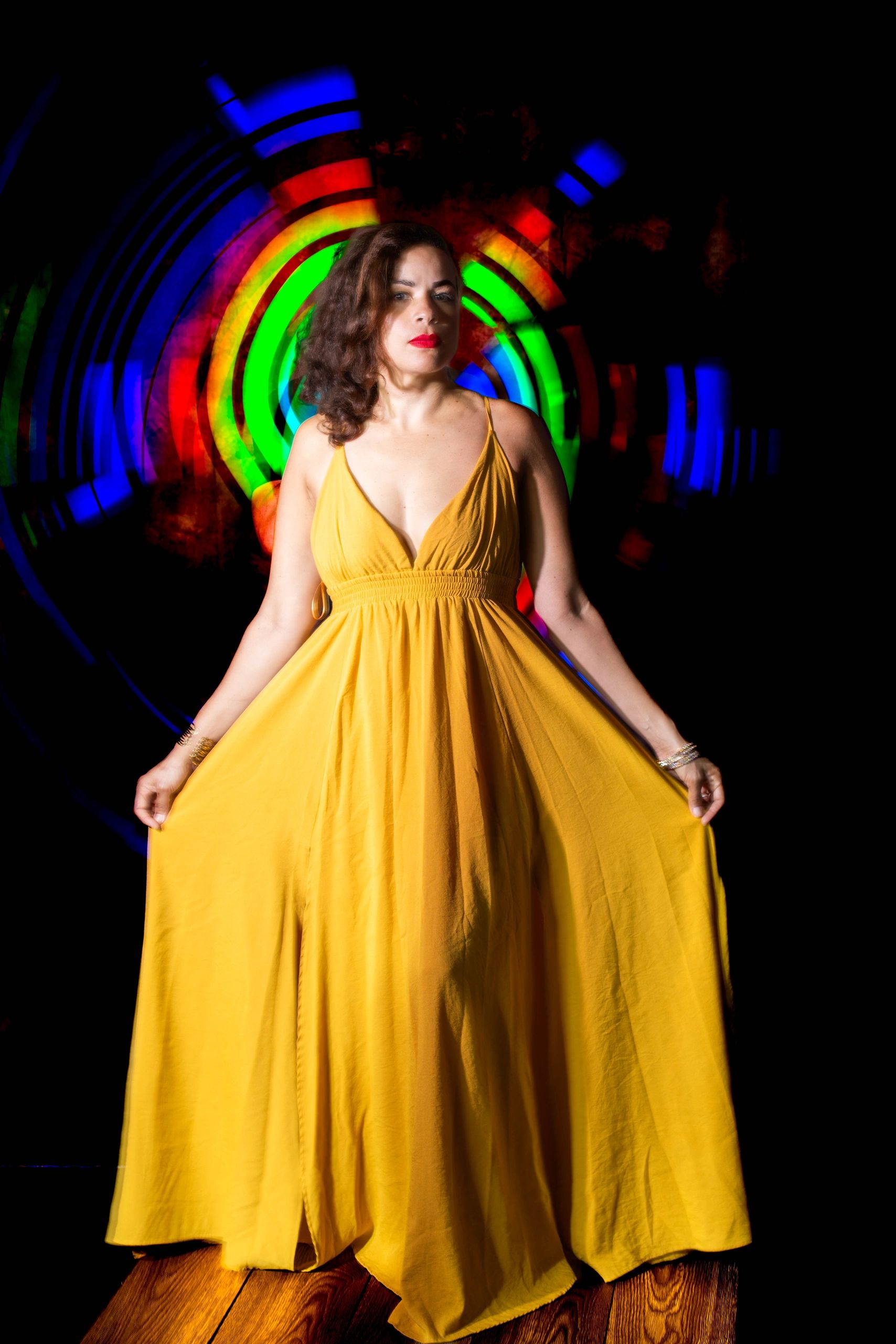 Woman in a flowing yellow dress stands against vibrant colorful light circles.
