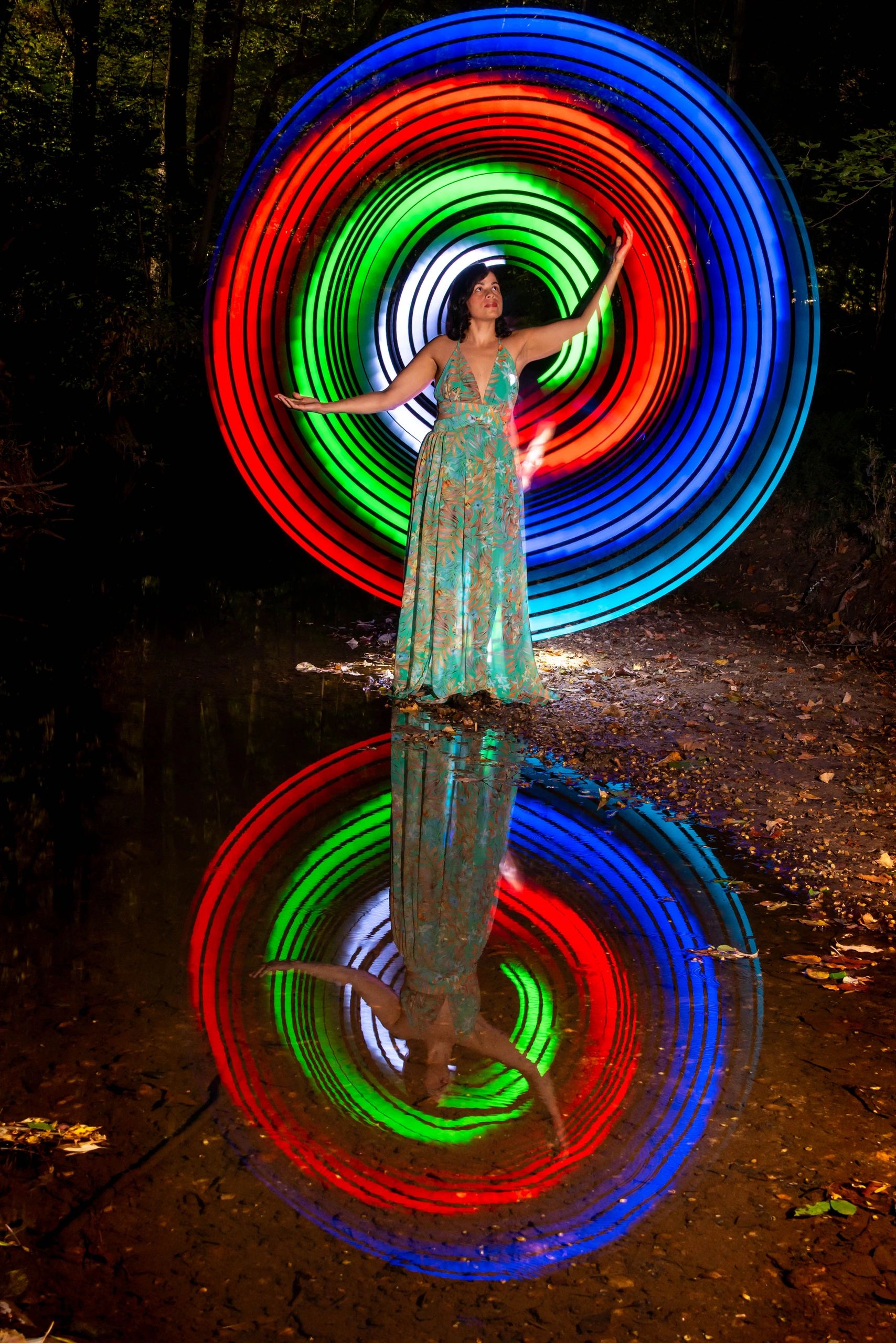 Woman in a colorful dress with vibrant light circles reflected in water.