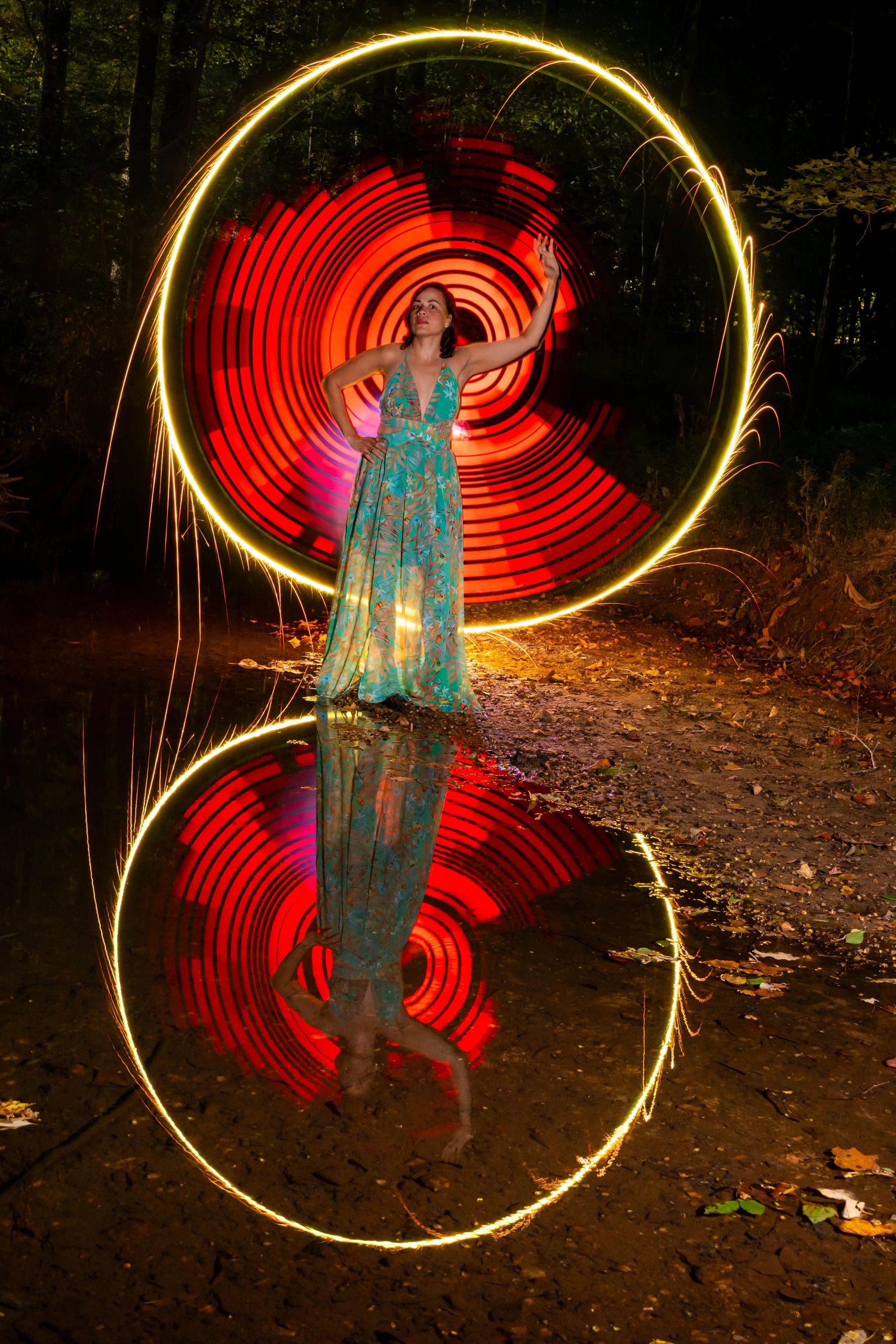 Woman in a long dress with glowing circular light patterns and reflection in water.