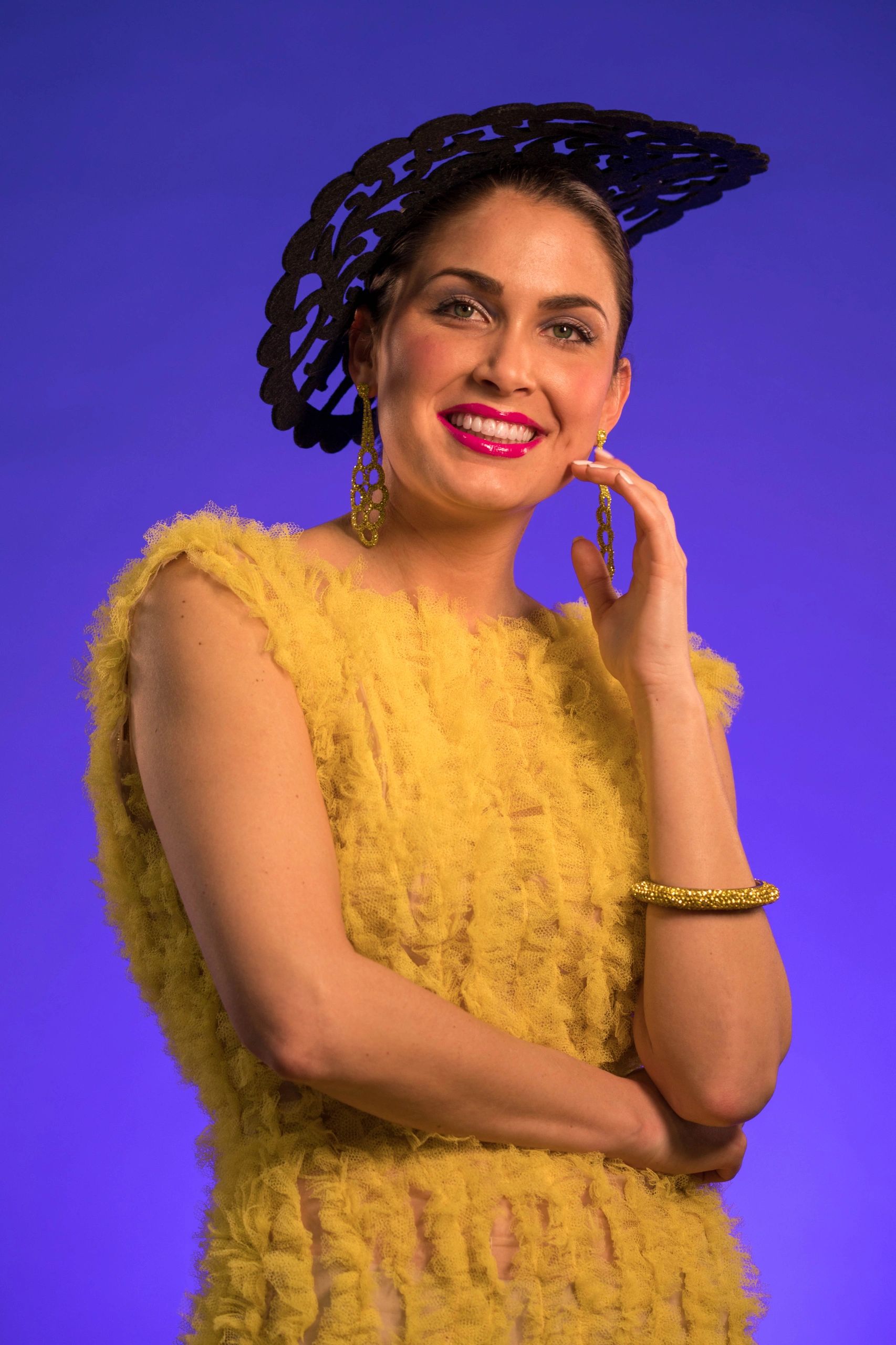 Smiling woman in a textured yellow dress and black headpiece against a purple background.