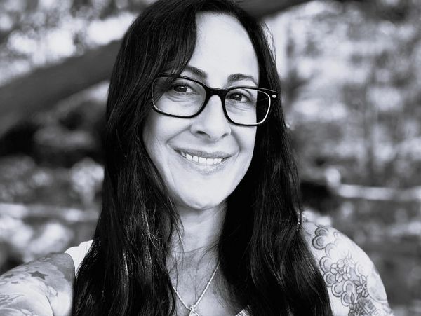 Smiling woman with glasses and tattoos in a black and white photo.