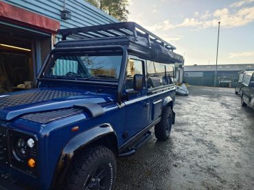 Blue off-road vehicle parked outside a workshop during sunset.