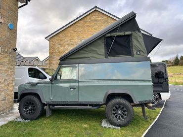 Green off-road vehicle with a raised rooftop tent parked on grass.