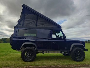 A dark off-road vehicle with a raised tent roof parked on grass.