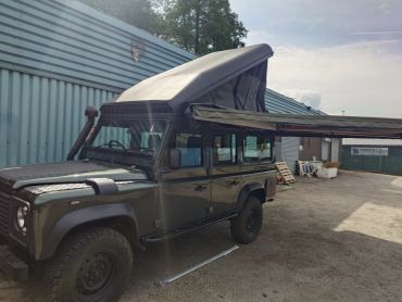 Off-road vehicle with a pop-up roof and side awning setup outdoors.